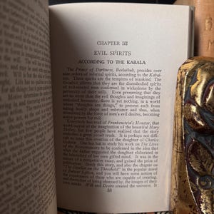 May include: Open book with text about evil spirits and the Kabala. The page is from an older book with aged paper. A decorative gold-colored object is visible on the right side of the image.