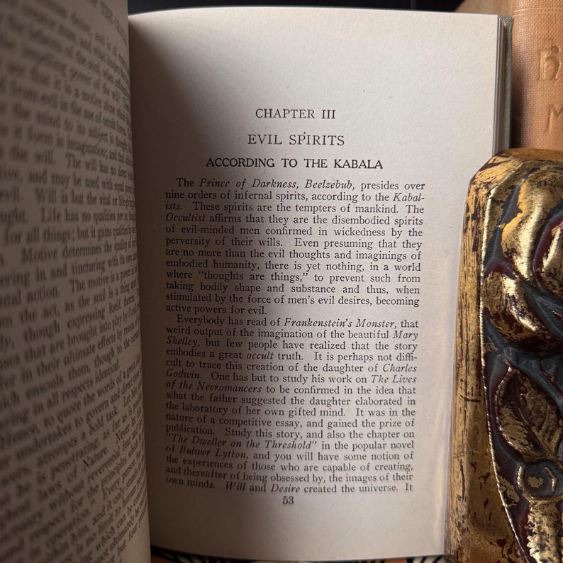 May include: Open book with text about evil spirits and the Kabala. The page is from an older book with aged paper. A decorative gold-colored object is visible on the right side of the image.