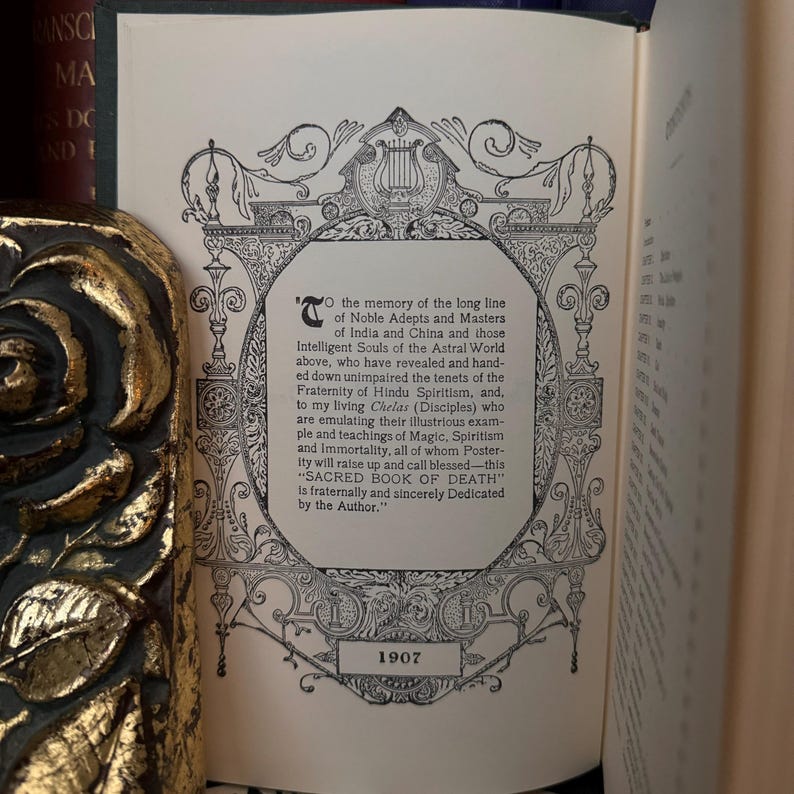 May include: A black and white image of a book page with an ornate border. The text on the page is a dedication to the memory of "Noble Adepts and Masters" of India and China. The text also mentions "SACRED BOOK OF DEATH" and the year 1907.