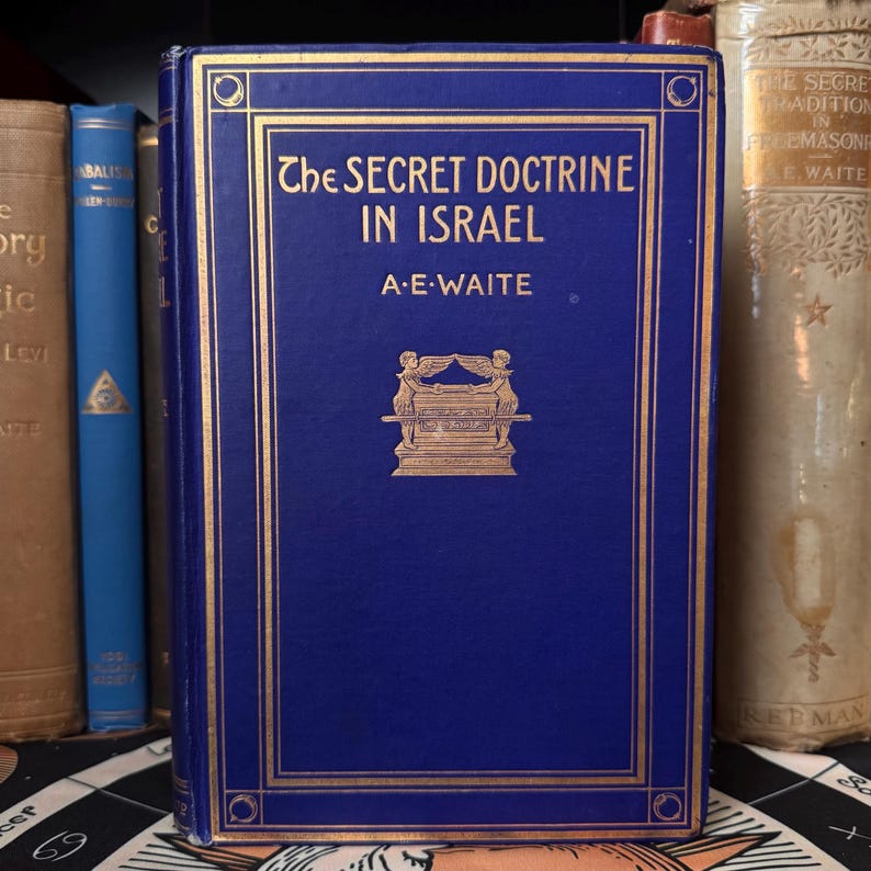 May include: A dark blue hardcover book titled "The Secret Doctrine in Israel" by A.E. Waite, with gold lettering and a gold illustration. Other books are visible in the background, suggesting a collection.