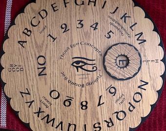 May include: A wooden Ouija board with a scalloped edge, featuring letters, numbers, and phrases like "yes" and "no." The planchette is a small, round piece with a central hole. The board has the text "Third Eye Concepts" and "Talking Board Set."