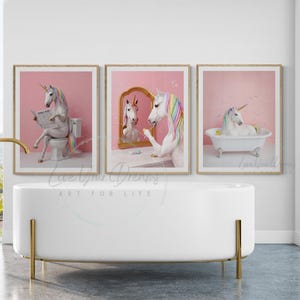 May include: Three framed wall art prints featuring a white unicorn with a rainbow mane and tail. The first shows the unicorn on a toilet reading a newspaper, the second applying makeup in a gold mirror, and the third relaxing in a bathtub.