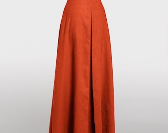 May include: A high-waisted, floor-length skirt in a solid burnt orange color. The skirt features a structured waistband and a prominent vertical inverted pleat running down the center front, creating a flared, A-line silhouette with clean lines.