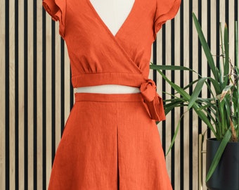 Peut inclure: Une tenue deux pièces de couleur orange brûlée. Le haut est un style enveloppant court avec des manches à volants. La jupe est une mini-jupe avec un devant plissé.