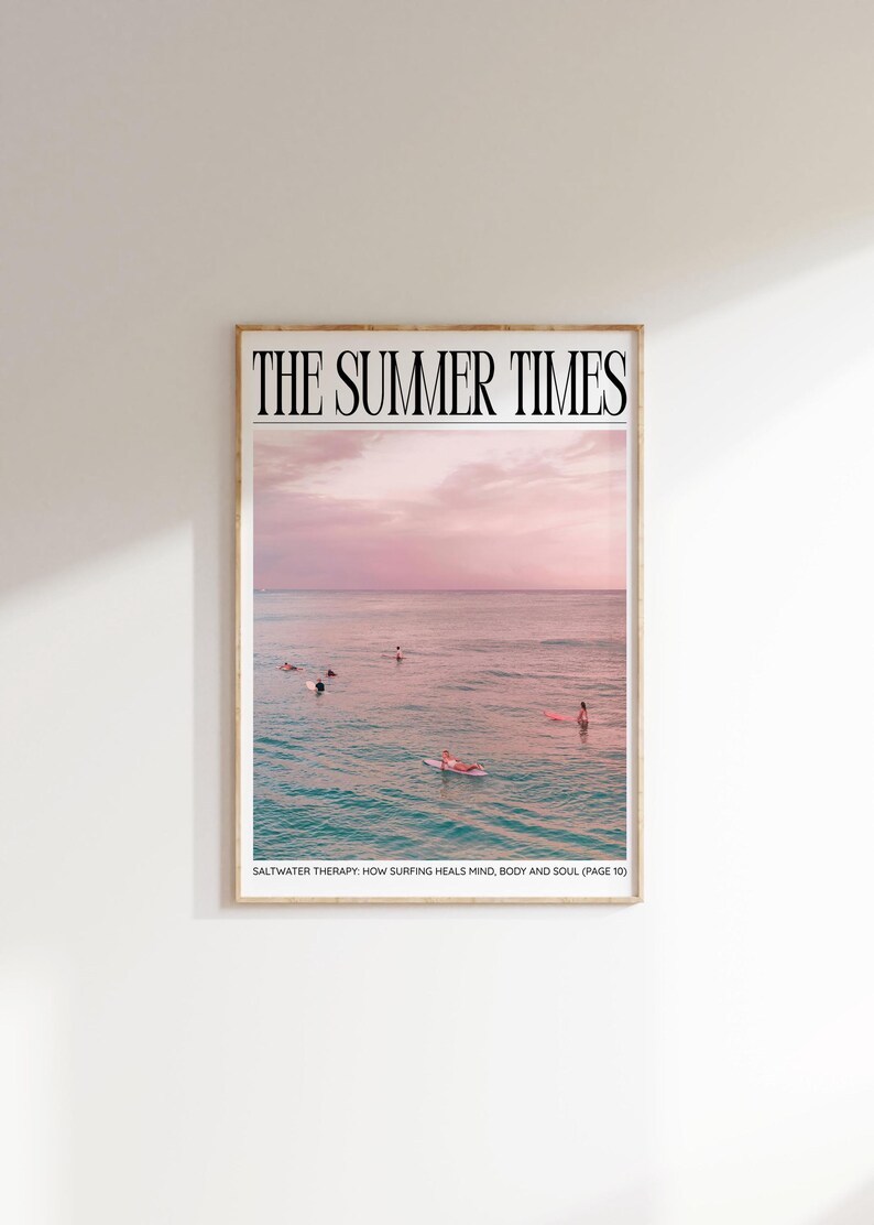 May include: A framed print featuring a serene ocean scene under a pink and purple sky. The text "THE SUMMER TIMES" is at the top. Surfers are in the water. The text "SALTWATER THERAPY: HOW SURFING HEALS MIND, BODY AND SOUL (PAGE 10)" is at the bottom.