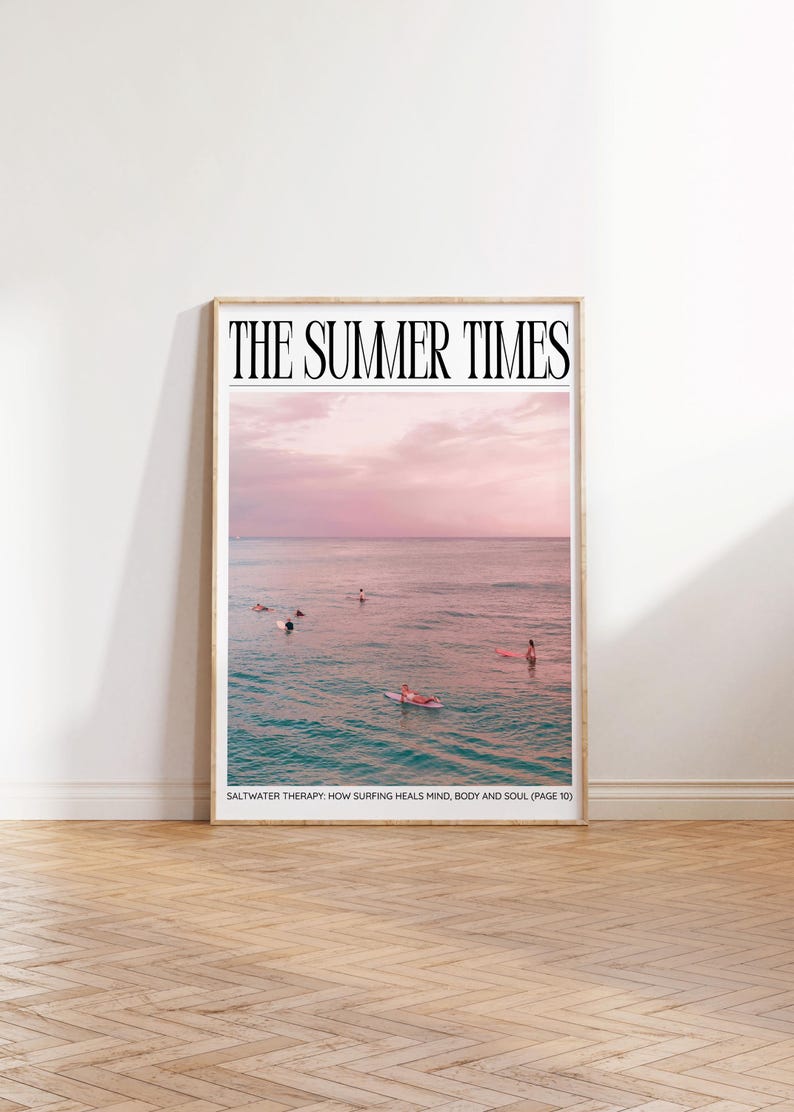 May include: Framed print featuring a serene ocean scene with surfers. The sky transitions from pink to blue, with the text "THE SUMMER TIMES" at the top. The caption reads "SALTWATER THERAPY: HOW SURFING HEALS MIND, BODY AND SOUL (PAGE 10)".