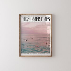May include: A framed print featuring a serene ocean scene under a pink and purple sunset sky. The text "THE SUMMER TIMES" is at the top, with "SALTWATER THERAPY: HOW SURFING HEALS MIND, BODY AND SOUL (PAGE 10)" at the bottom. Surfers are visible in the water.