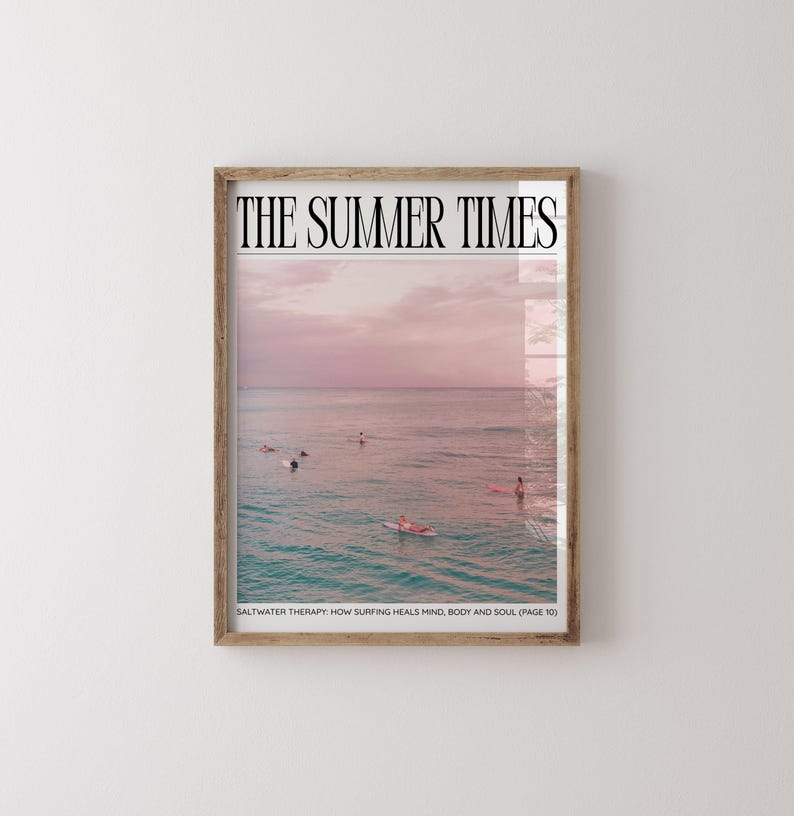 May include: A framed print featuring a serene ocean scene under a pink and purple sunset sky. The text "THE SUMMER TIMES" is at the top, with "SALTWATER THERAPY: HOW SURFING HEALS MIND, BODY AND SOUL (PAGE 10)" at the bottom. Surfers are visible in the water.