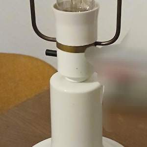 May include: A white ceramic table lamp with a large, clear light bulb. The lamp has a cylindrical base with a blue and white design. The lamp is approximately 12 inches tall.