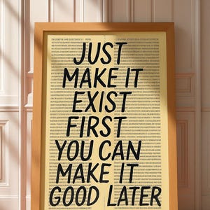 May include: A framed print with the text "JUST MAKE IT EXIST FIRST YOU CAN MAKE IT GOOD LATER" in bold black letters. The background is a light yellow color with small text. The frame is a light brown color.
