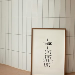 May include: A framed print with the text "I think I like this little life" in black handwritten font on a white background. The frame is brown wood.