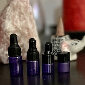 May include: Four small glass bottles with black caps and purple liquid inside. The bottles are lined up in a row on a dark surface.