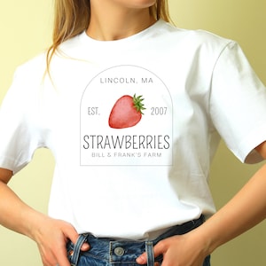 May include: White t-shirt with a black and white logo that says "Strawberries Bill & Frank's Farm" with a red strawberry illustration and the text "Lincoln, MA Est. 2007".