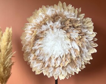 May include: A floor lamp with a large, round shade made of white and tan feathers. The lamp has a dark metal pole and stands against a terracotta-colored wall. Dried pampas grass is in a basket to the left.