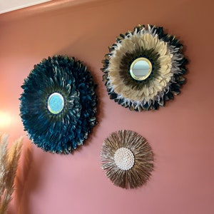 May include: Three decorative wall mirrors. Two are circular, with feather-like textures in teal and cream colors, and a smaller one with a gold and white sunburst design. All have a mirror in the center, and are mounted on a pink wall.