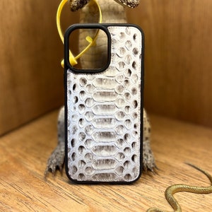 Puede incluir: Una funda rectangular para smartphone con un patrón texturizado de piel de serpiente en color blanco roto y gris en el panel posterior, enmarcado por un borde negro sólido. La funda incluye un gran recorte cuadrado para la cámara.