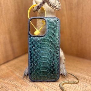 Może przedstawiać: Ciemnozielone etui na telefon z teksturowanym wzorem wężowej skóry i czarną ramką. W górnej części etui widoczny jest jaskrawożółty, okrągły pierścień. Etui posiada prostokątne wycięcie na obiektyw aparatu na tylnej stronie.