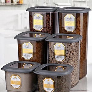 May include: Six clear plastic square storage containers with grey lids. The containers are filled with various dry goods, such as pasta, beans, and sugar. The containers have labels with the words "Luxury Products" and the names of the contents in gold lettering. The containers are labelled with the following: "Tel Schriye", "Makarna", "Kuru Fasulye", "Sefer", "Kekik". The containers are labelled with the following sizes: 1750 ml, 1200 ml, and 550 ml.