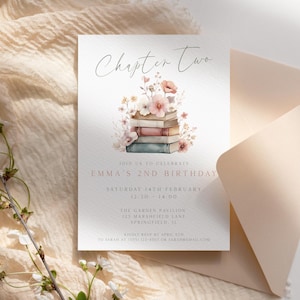 Puede incluir: Una tarjeta de invitación de cumpleaños con el texto "Chapter Two" y detalles del segundo cumpleaños de Emma. La tarjeta presenta una ilustración de acuarela de libros y flores. Una sobre está al lado de la tarjeta, y una ramita de flores está en primer plano.