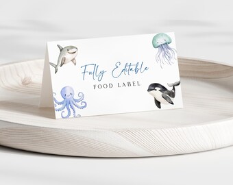 May include: A white, folded food label with watercolor illustrations of sea creatures. The label features a smiling shark, octopus, orca, and jellyfish. The text "Fully Editable FOOD LABEL" is written in a blue script font.