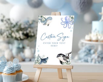 May include: A white custom sign on a wooden easel, featuring watercolor illustrations of marine animals like a whale, octopus, stingray, and orca. The sign reads "Custom Sign" and "Enter your text here!" in blue script.