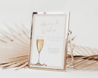 May include: A silver picture frame with a white card inside. The card has a pink border and gold text that reads "Advice & Wishes for the Soon to Be Mrs." There is a drawing of a champagne flute with gold bubbles and pearls on the bottom of the card.