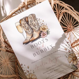 Puede incluir: Una invitación a una despedida de soltera con una ilustración de acuarela de botas de vaquero y una copa de champán. El texto dice "Boots and Bubbly" y "Please join us in celebrating the bride to be Amelia Greyson".