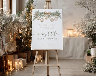 May include: A white sign on a wooden easel, featuring a Christmas design. The sign says "Welcome to Victoria's merry little baby shower" with the date 14.12.2025. The top of the sign has a garland with baubles and a bow, perfect for a baby shower.