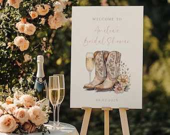 Könnte beinhalten: Ein weißes Schild mit dem Text "Willkommen zu Amelias Bridal Shower" in rosa Schrift. Das Schild zeigt außerdem eine Aquarell-Illustration von zwei Cowboystiefeln, einem Glas Champagner und Wildblumen. Das Datum "08.02.202X" ist unten auf dem Schild gedruckt.