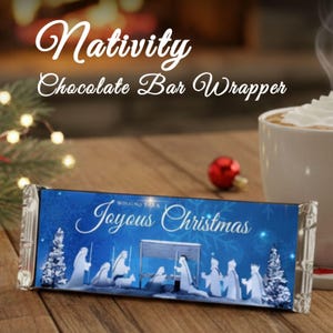 Op de afbeelding: Blauwe chocoladereepverpakking met de woorden "Nativity Chocolate Bar Wrapper" en "Joyous Christmas". De verpakking toont een kerststal met witte figuren en kerstbomen tegen een blauwe achtergrond. Op de achtergrond een kop koffie met slagroom.