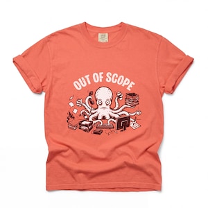 May include: Coral-colored t-shirt with rolled-up sleeves. The shirt features a cartoon octopus illustration with the text "OUT OF SCOPE" in white. The octopus is surrounded by office supplies, including a phone, computer, and stacks of paper.
