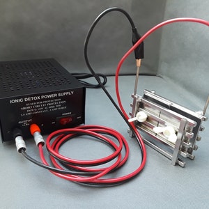 May include: A black ionic detox power supply with a red power switch and two output jacks. The power supply is connected to a silver metal plate with white plastic pieces and red and black wires.