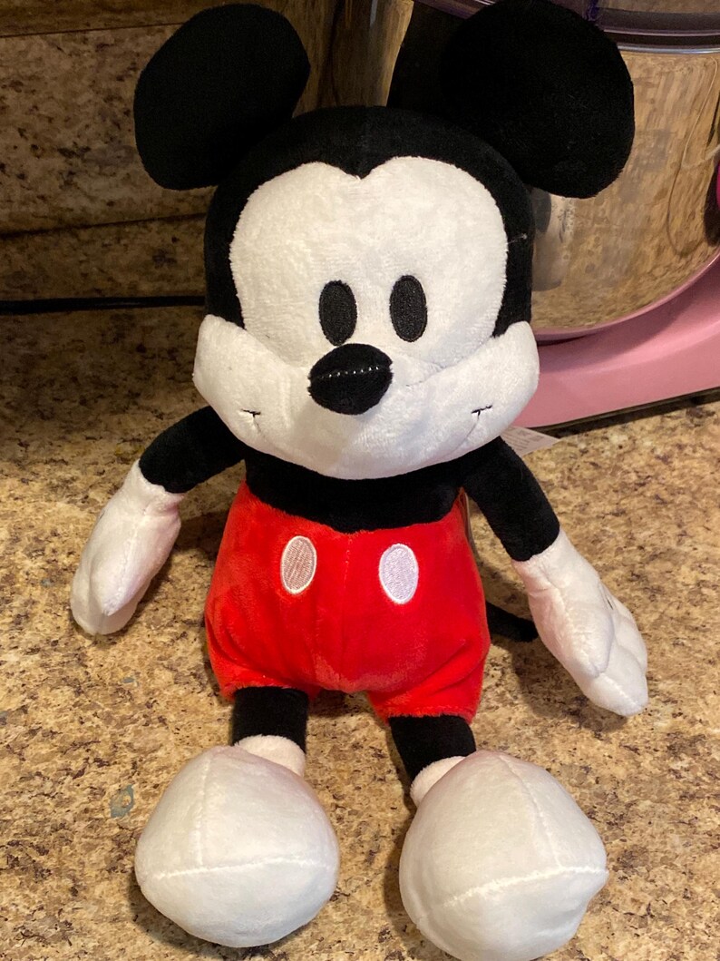 Puede incluir: Un peluche de Mickey Mouse. El juguete tiene una cara blanca, orejas negras y un cuerpo negro. Viste pantalones cortos rojos con botones blancos, guantes blancos y zapatos blancos. El dise&ntilde;o est&aacute; basado en el famoso personaje de Disney.