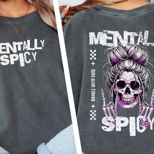 K&ouml;nnte beinhalten: Dunkelgraues T-Shirt mit den Worten "MENTALLY SPICY" in Wei&szlig;. Auf der R&uuml;ckseite befindet sich ein Totenkopf mit einem rosa Dutt und Skeletth&auml;nden, die eine Rock'n'Roll-Geste machen, mit dem Wort "SPICY" darunter.