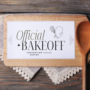 May include: A white sign with black text that reads "Official Bakeoff Convention Centre" on a wooden cutting board with a wooden spoon.