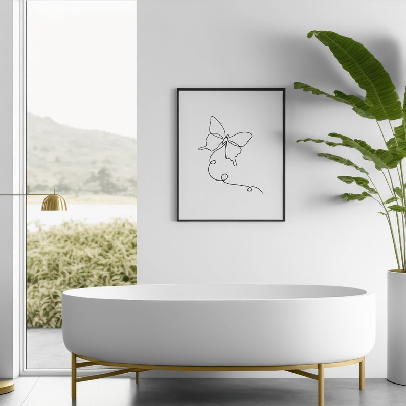 May include: A white bathtub with gold legs sits in a bathroom with a framed black and white line drawing of a butterfly on the wall. A potted plant is on the right side of the image.