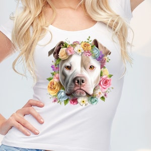 May include: White and brown pit bull terrier wearing a flower crown with pink, yellow, white, and purple flowers. The dog is looking directly at the camera.