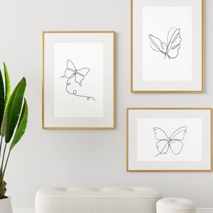 May include: Three framed prints with black line drawings of butterflies on a white background. The frames are gold.