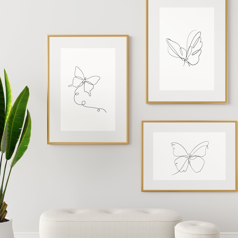 May include: Three framed prints with black line drawings of butterflies on a white background. The frames are gold.