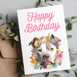 May include: Happy Birthday card featuring a white and brown pit bull wearing a flower crown. The flowers are pink, yellow, blue, and white.