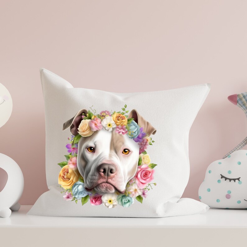 May include: White and brown pit bull terrier wearing a flower crown with pink, yellow, purple, and blue flowers. The dog is looking directly at the camera. The image is on a white pillow.