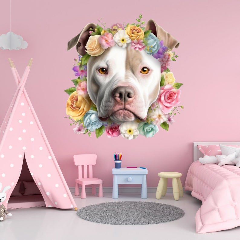 May include: A white and brown pit bull terrier wearing a colorful flower crown. The dog is looking directly at the camera. The background is a light pink wall.