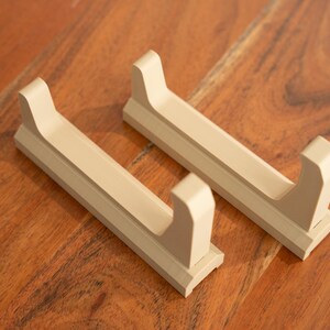 May include: Two beige plastic wall-mounted holders for displaying items like swords or other long objects.