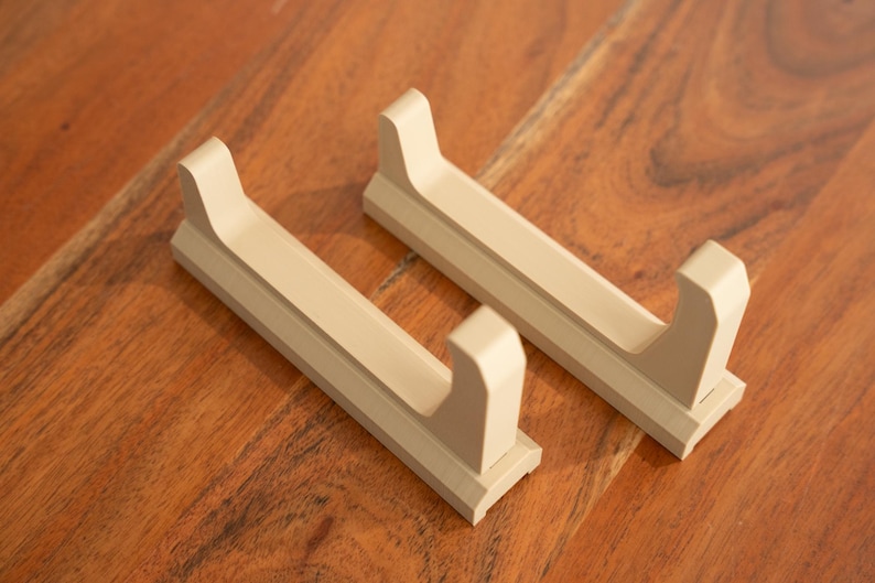 May include: Two beige plastic wall-mounted holders for displaying items like swords or other long objects.