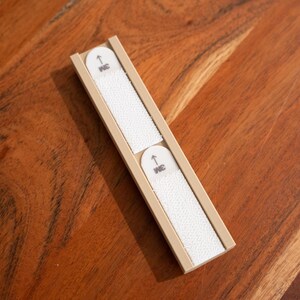 May include: Two white nail files are held in a beige plastic case. The case has a small arrow pointing up and the word "INC" printed on it.