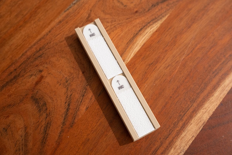 May include: Two white nail files are held in a beige plastic case. The case has a small arrow pointing up and the word "INC" printed on it.