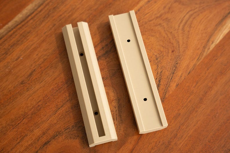 May include: Two beige plastic wall mount brackets with three holes each. The brackets are designed to hold a shelf or other object.