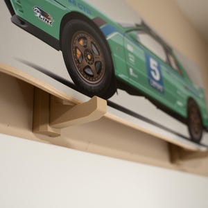 May include: A wooden wall mount with a hook for hanging a skateboard. The skateboard has a green and white design with a race car image and the number "5" on it.