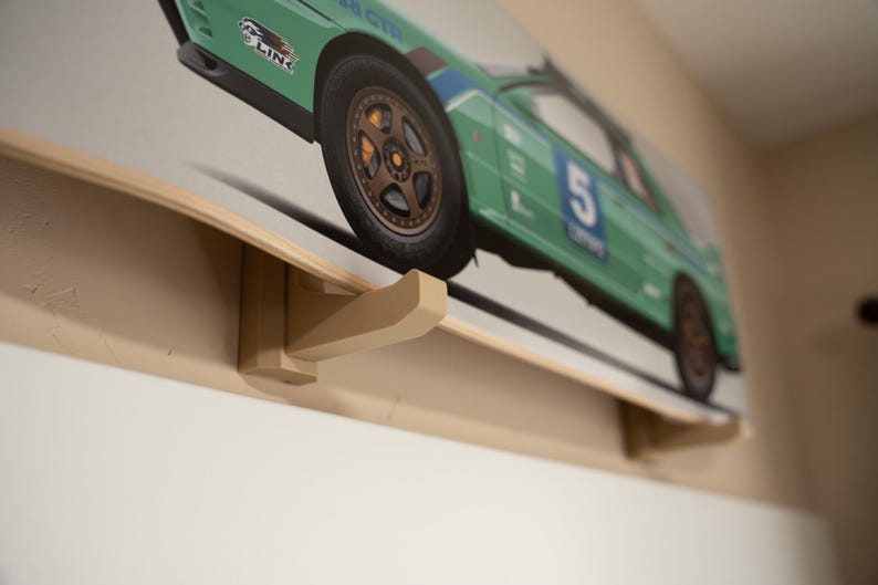 May include: A wooden wall mount with a hook for hanging a skateboard. The skateboard has a green and white design with a race car image and the number "5" on it.