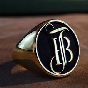 This product image features a personalized initial signet ring with a beautifully engraved monogram on its front surface. The ring’s classic oval shape and polished finish make it a timeless accessory for both men and women. Shown in Gold Plated, 14k Gold, and Silver options, it suits different style preferences. The detailed engraving highlights the initials with accuracy, making the ring ideal as a meaningful holiday or Christmas gift for someone special.